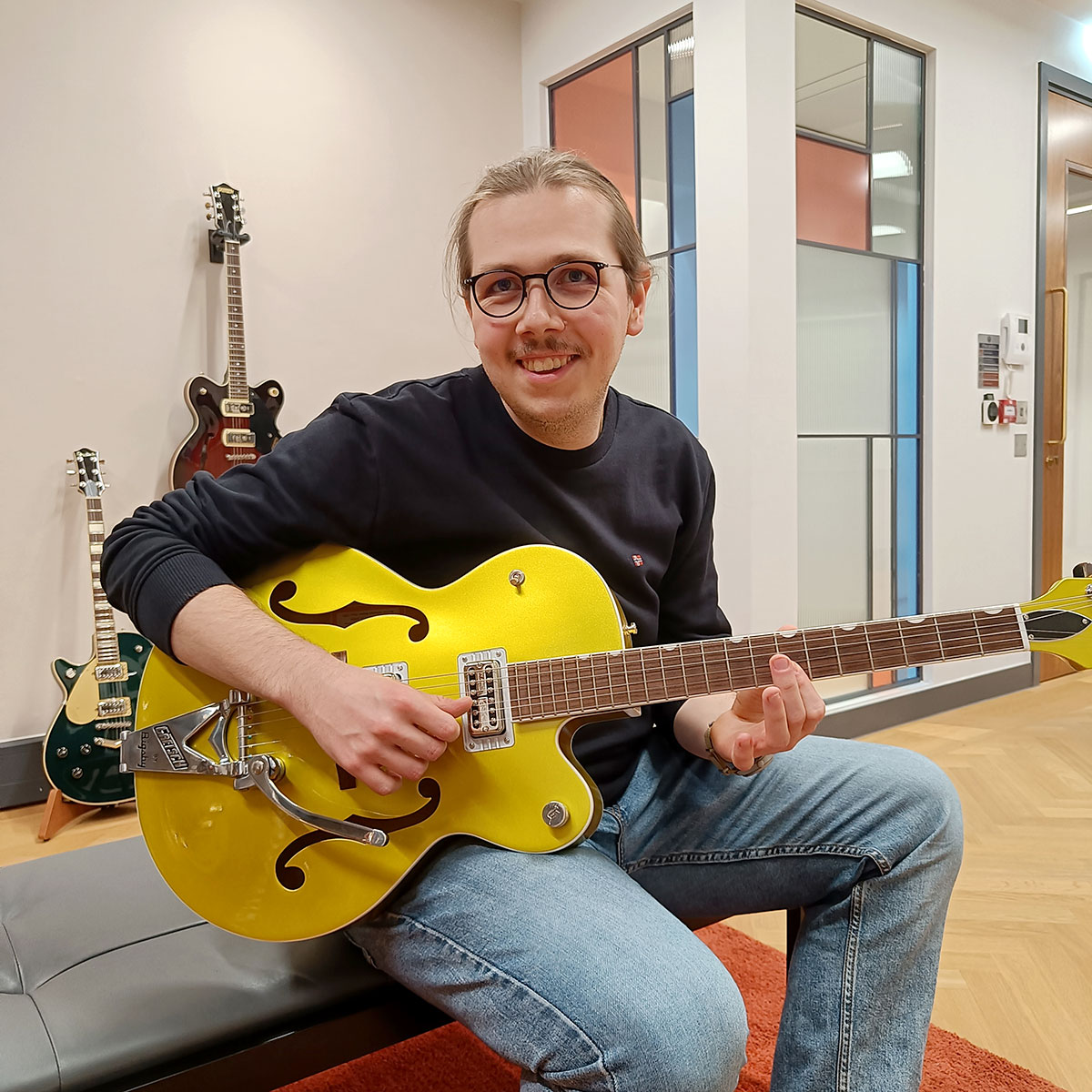 Kollege Nico sitzt auf einer gepolsterten Bank und spielt eine gelbe Gretsch-Gitarre
