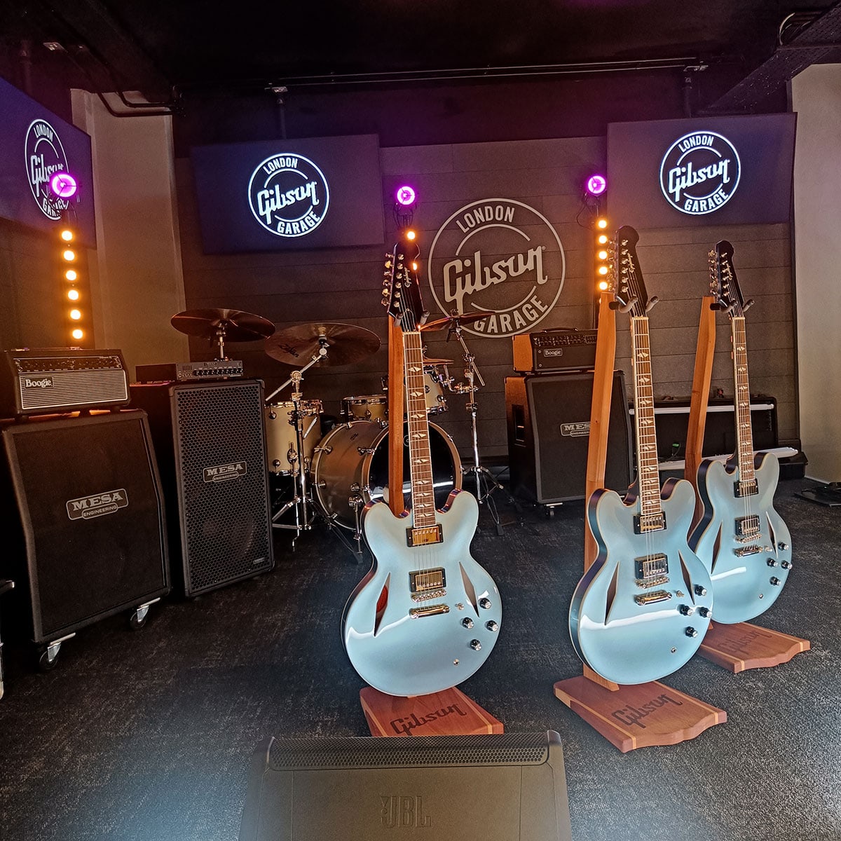 Gibson-Gitarren auf einer kleinen Bühne in der Gibson Garage. Im Hintergrund Schlagzeug und Boxen.