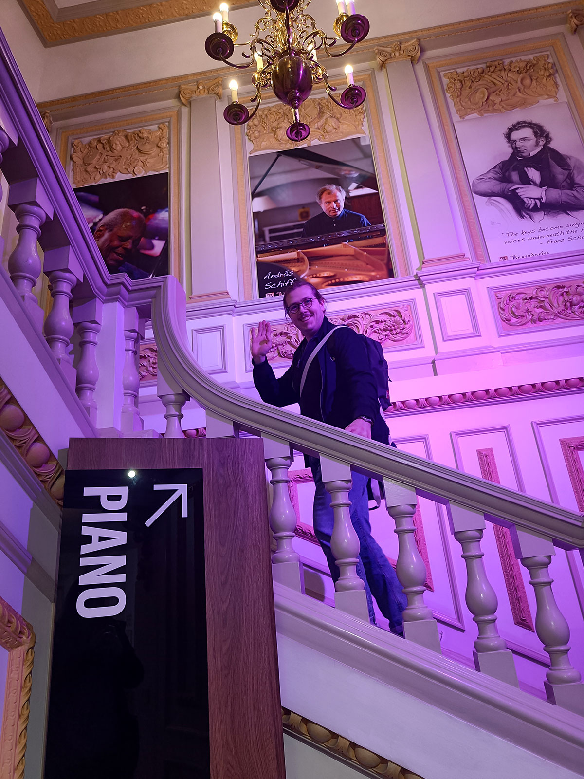 Kollege Nico im Innern des Yamaha-Stores in London. Er steigt eine dicke geschwungene barocke Treppe hinauf, im Vordergrund das Hinweisschild Piano.