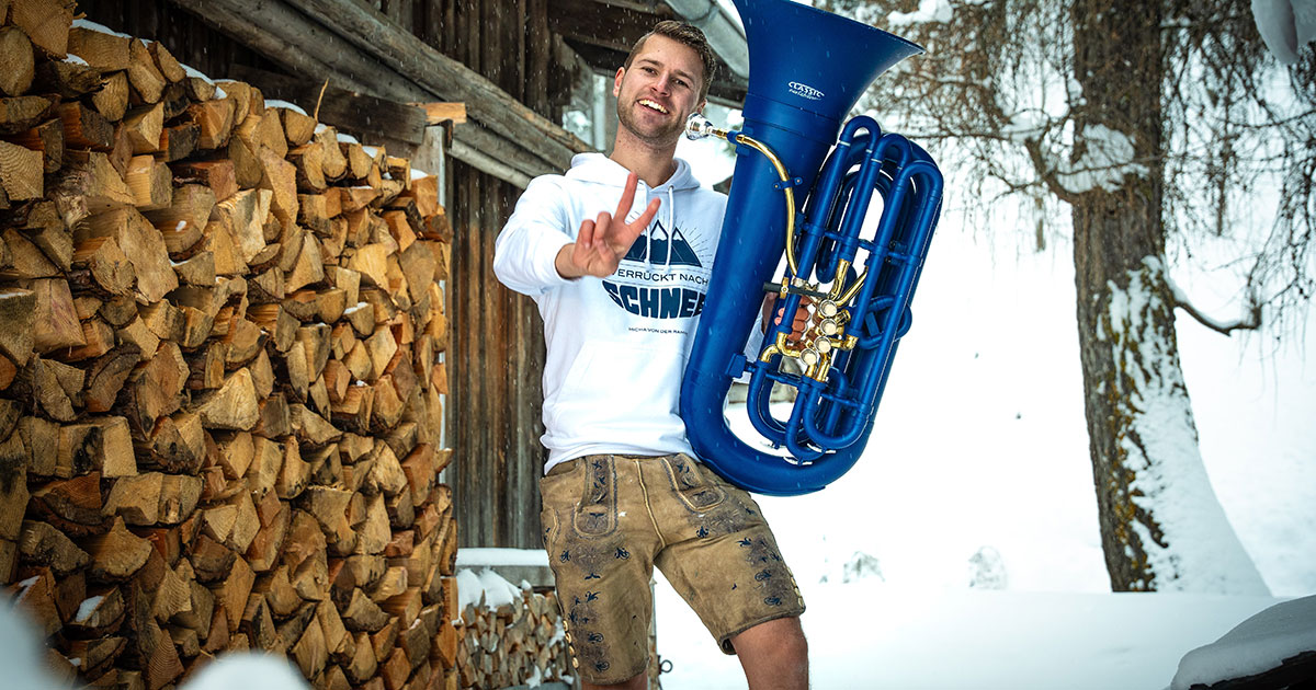 Micha von der Rampe mit unserer blauen MardiBrass-Tuba in verschneiter Landschaft vor einer Berghütte.