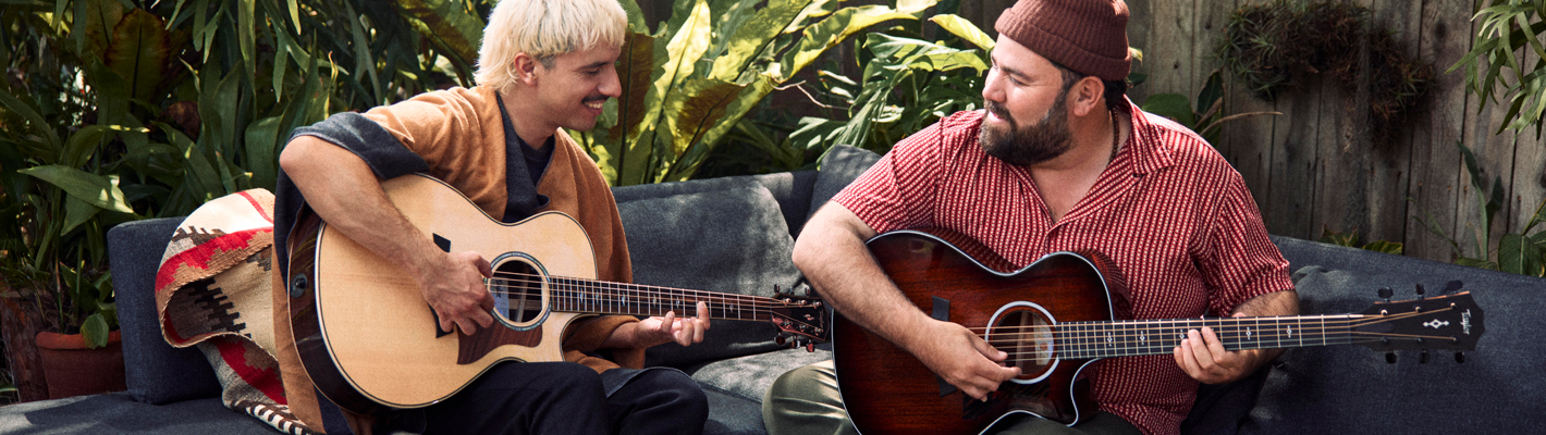 Two male musicians playing their new Taylor Next Generation acoustic guitars together on a terrace in a summery atmosphere and smiling happily