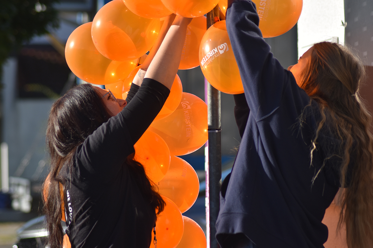 MusiConnect 2024: Mitarbeiterinnen von Kirstein beim Aufhängen von orangefarbenen Luftballons mit Kirstein-Logo