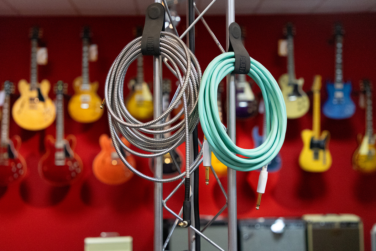 im Hintergrund E-Gitarren an einer Wand, im Vordergrund Kabel für E-Gitarren